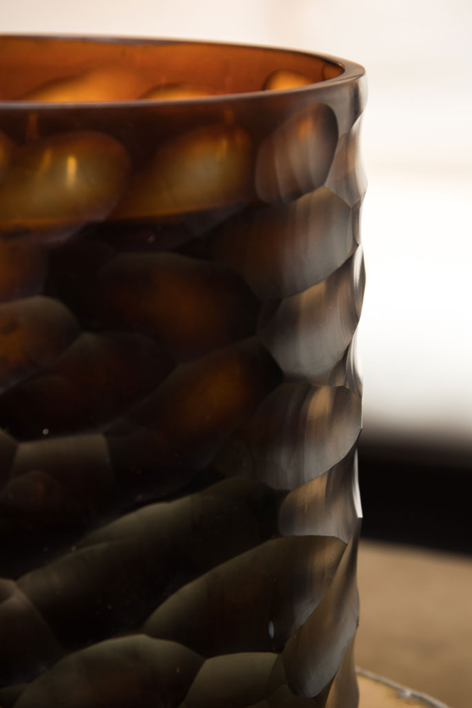 Close up detail of an amber-coloured glass t-light holder with organic cutting pattern.